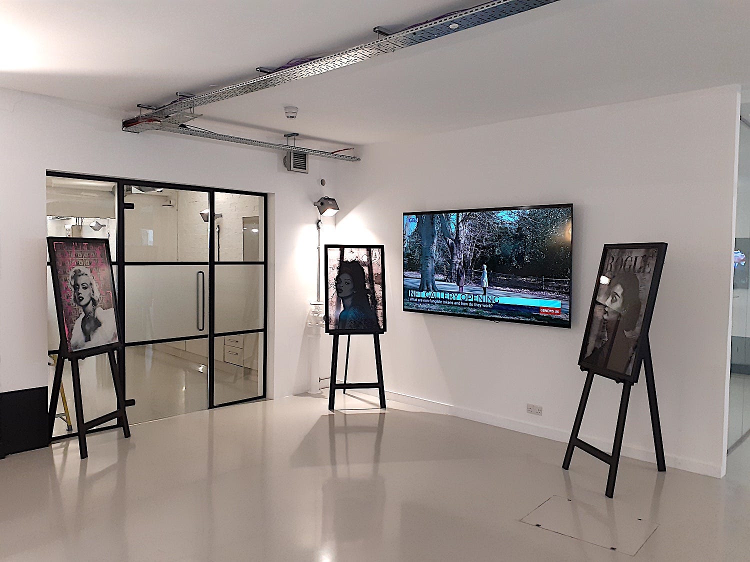 Three easels are positioned around a TV, showing a news report about the gallery's opening.