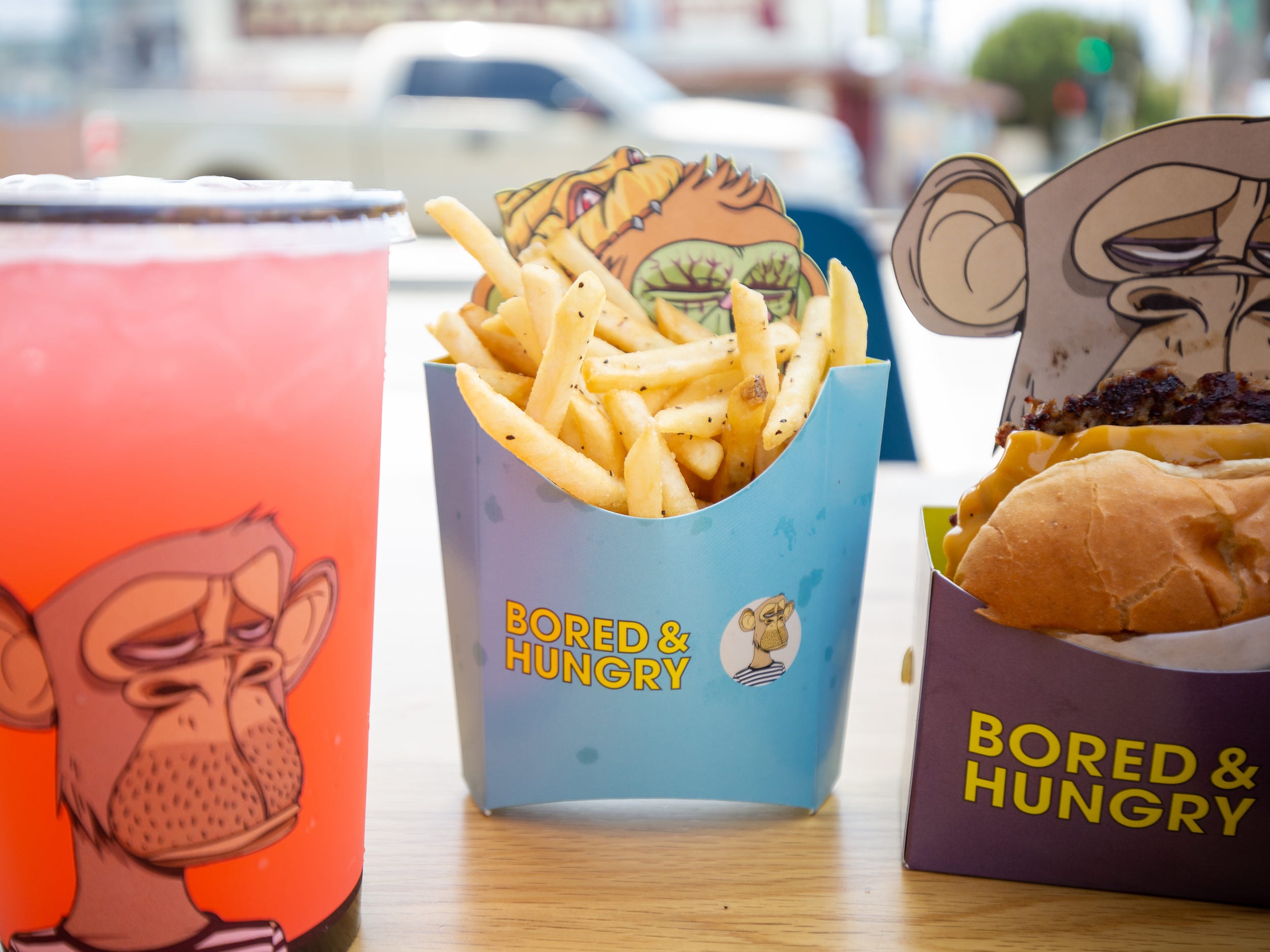 Burgers, fries, a pink drink all in ape branded Bored and Hungry packaging.