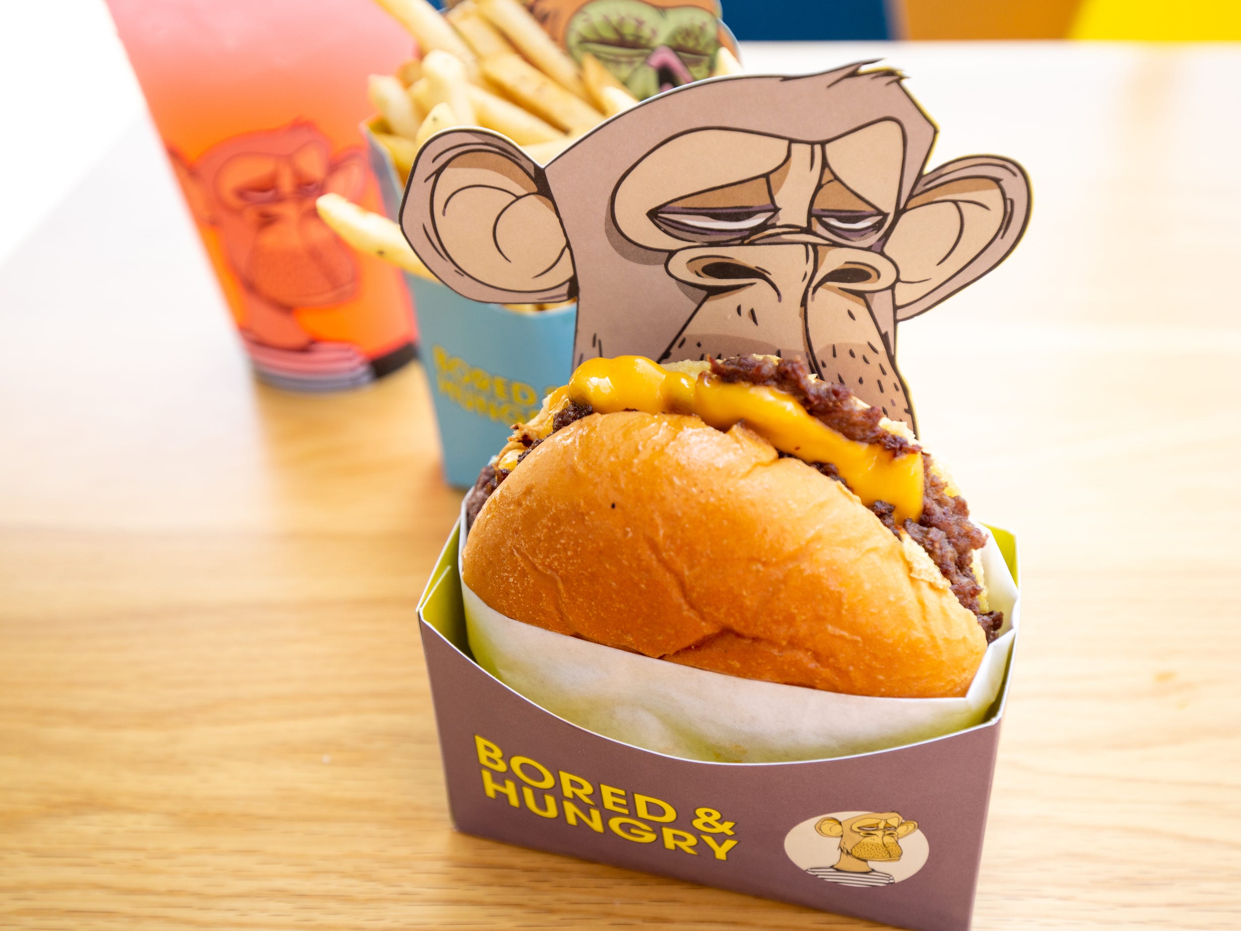 Burgers, fries, a pink drink all in ape branded Bored and Hungry packaging.