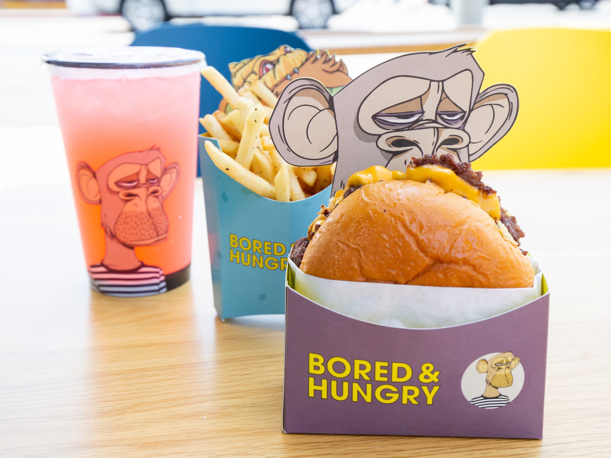 Burgers, fries, a pink drink all in ape branded Bored and Hungry packaging.