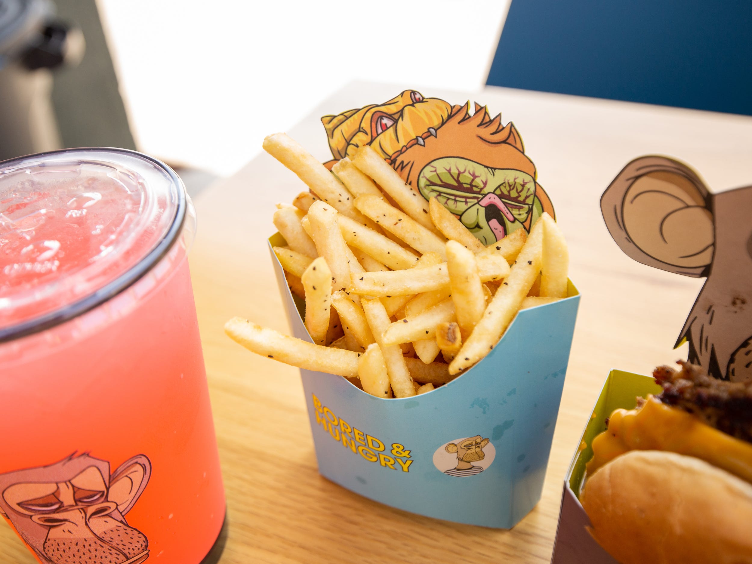 Burgers, fries, a pink drink all in ape branded Bored and Hungry packaging.