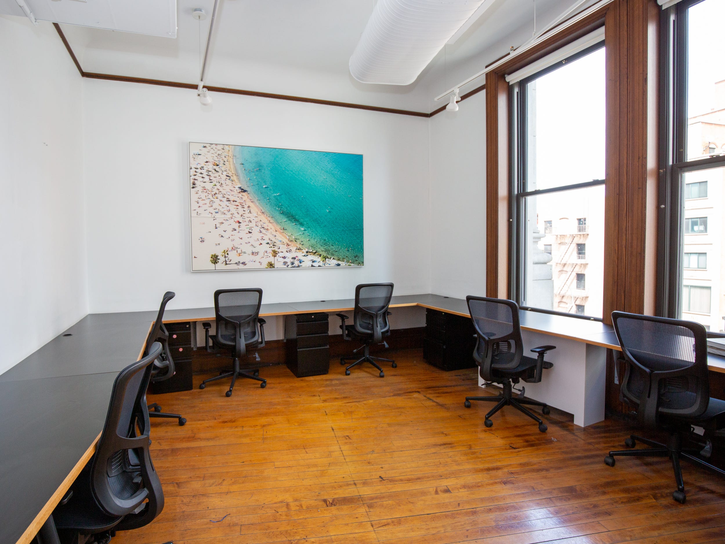 Long desks with office chairs, windows with views of nearby buildings, and art on the wall