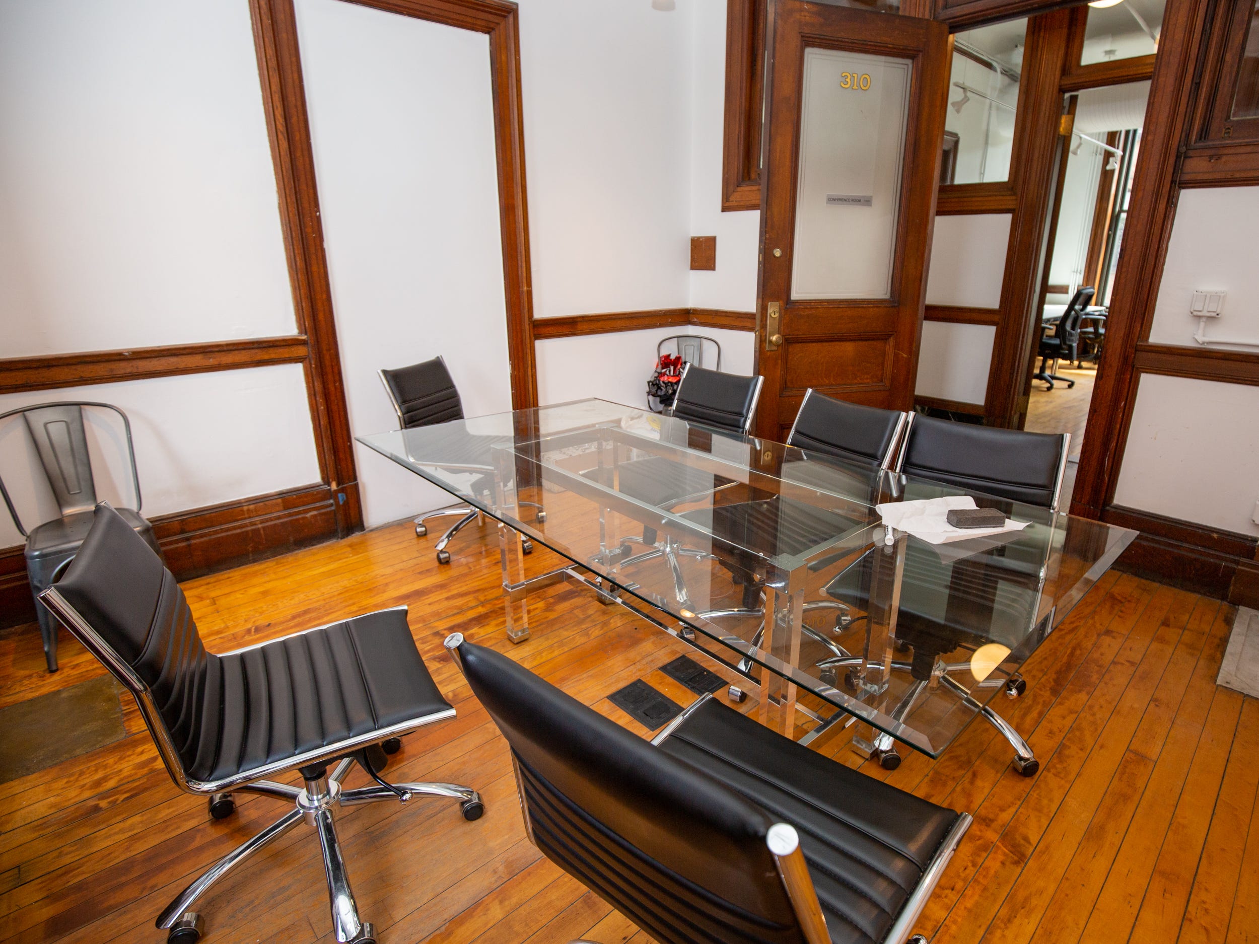 A glass table with office chairs near a hallway.