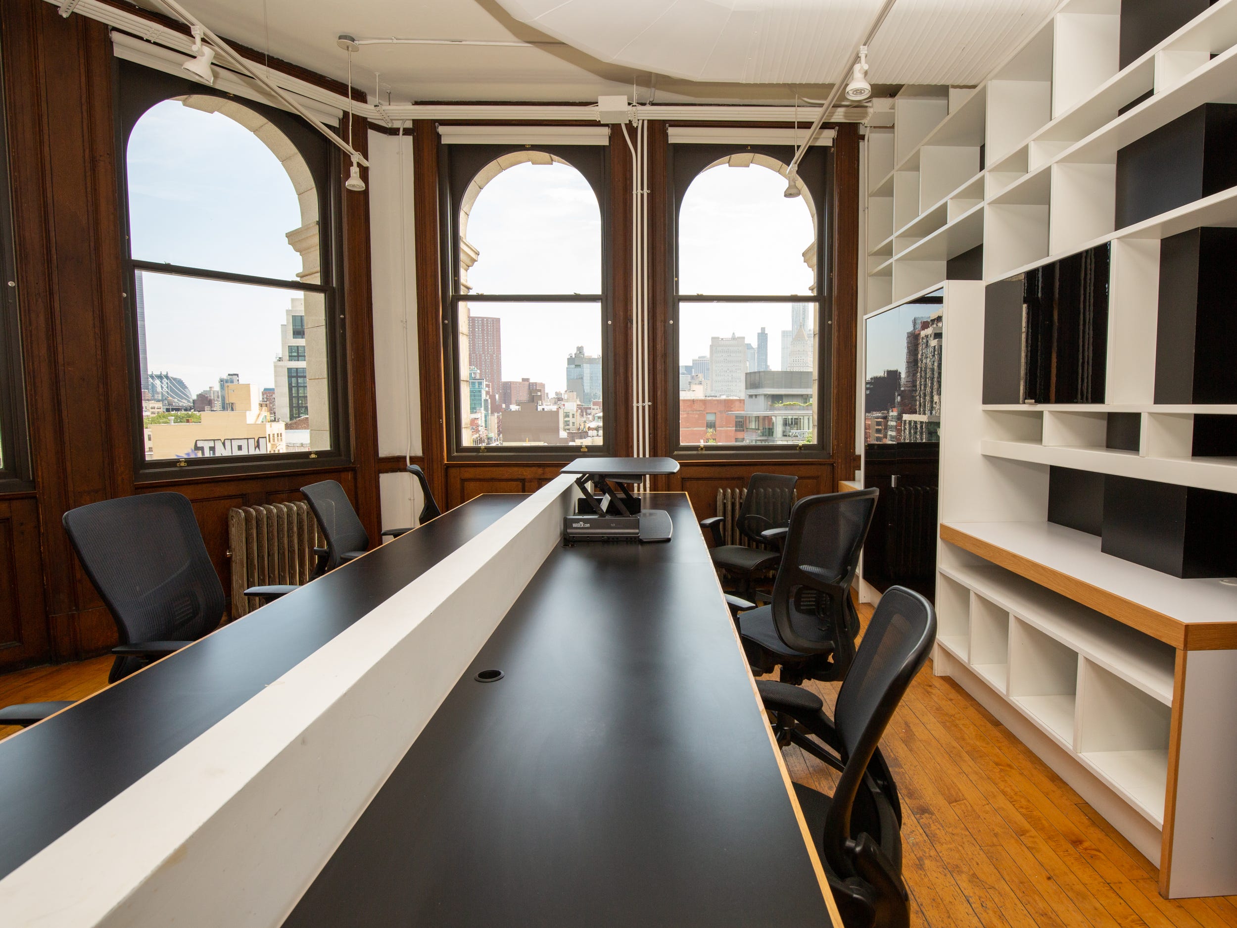 Long tables and office chairs near shelves and large windows.