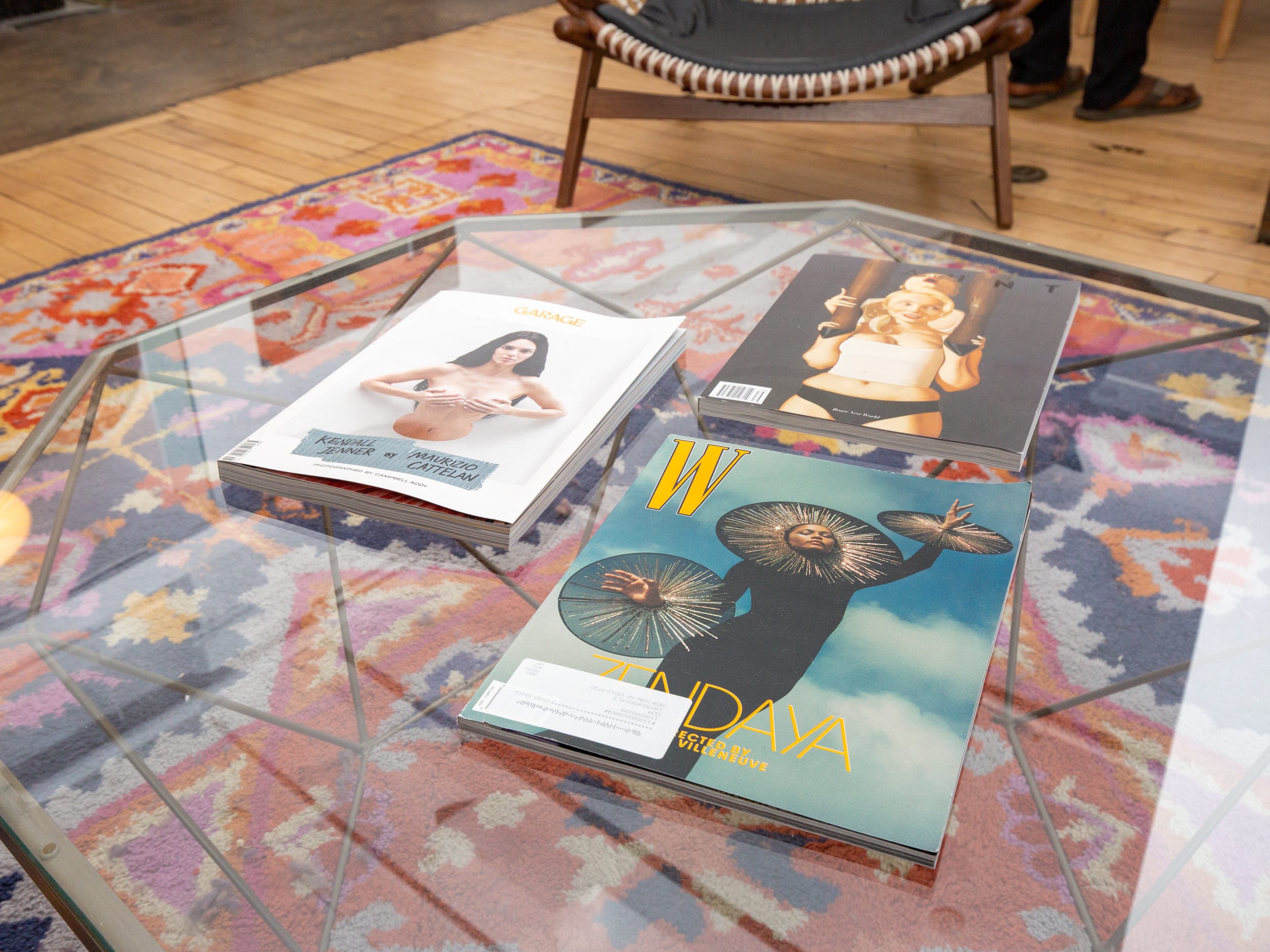 A glass table with magazines above a colorful rug.