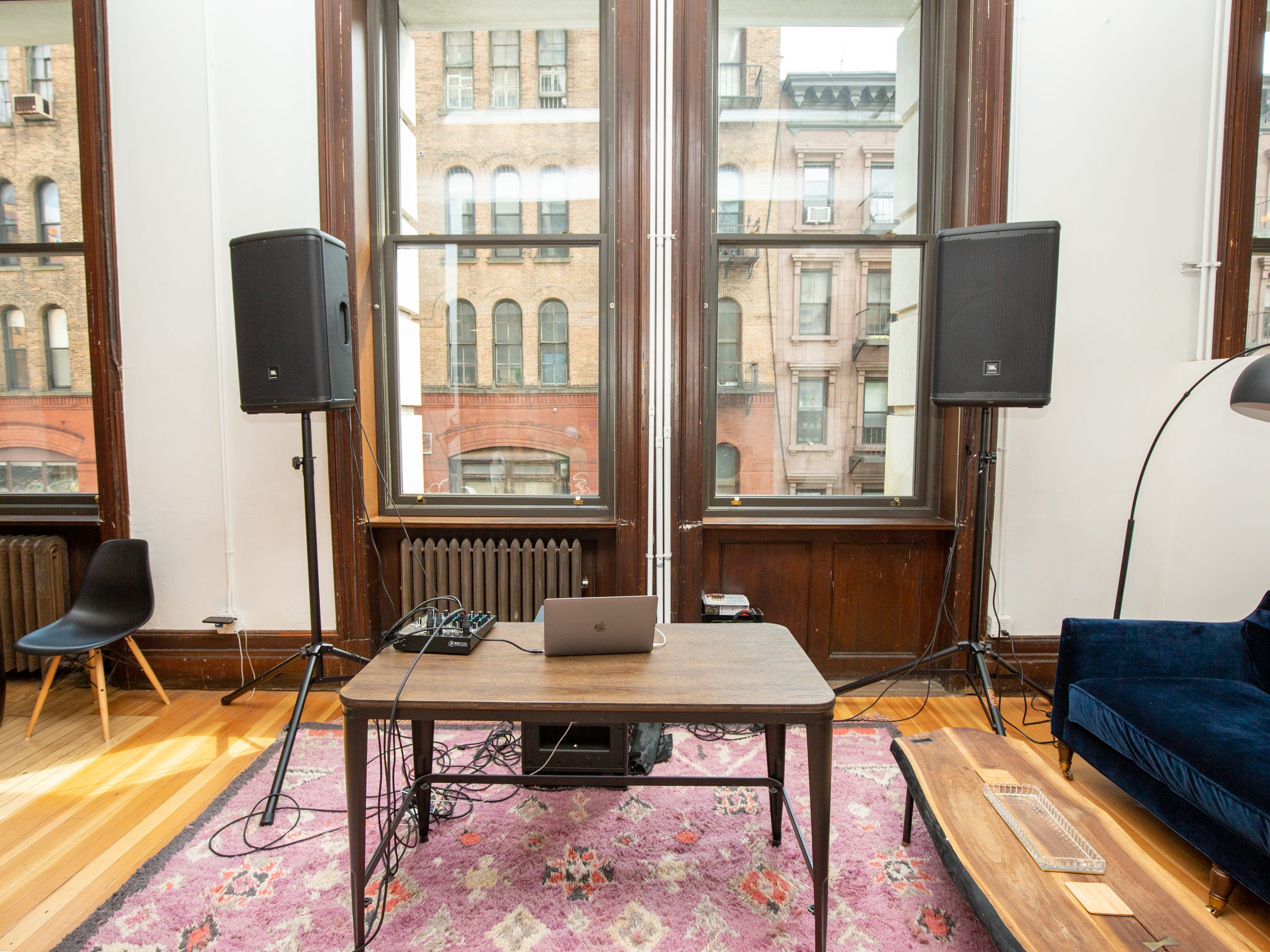 A table on a colorful rug with a table and chair and two speakers.