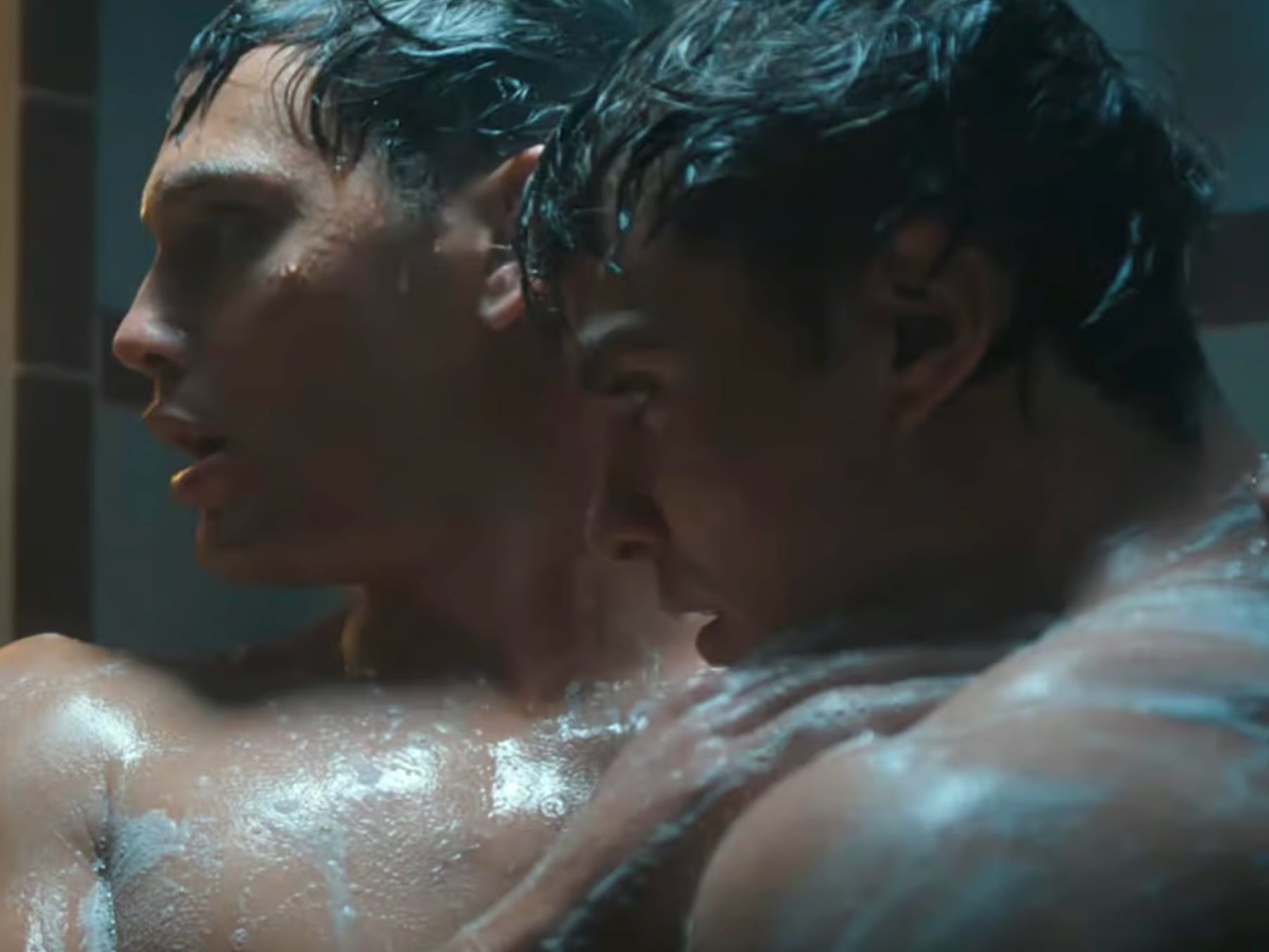 Two young men with dark hair holding each other in a shower, covered in soap.