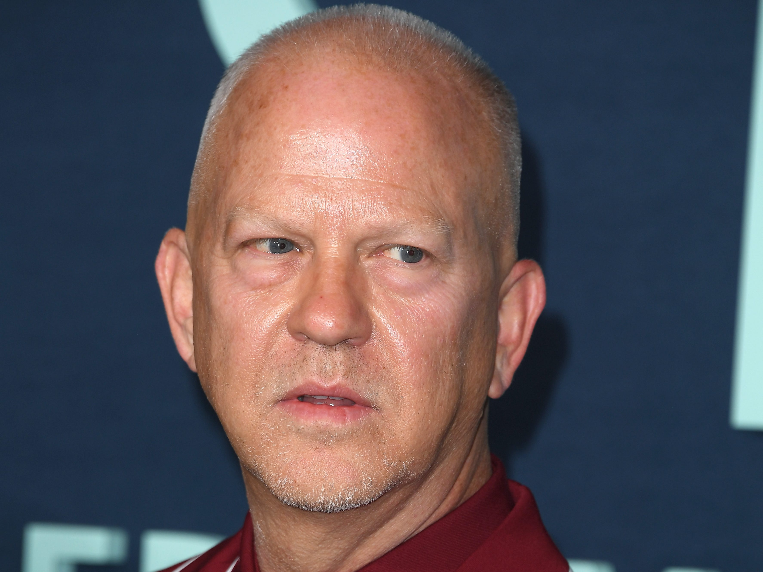 A man with short gray hair in a dark red suit.