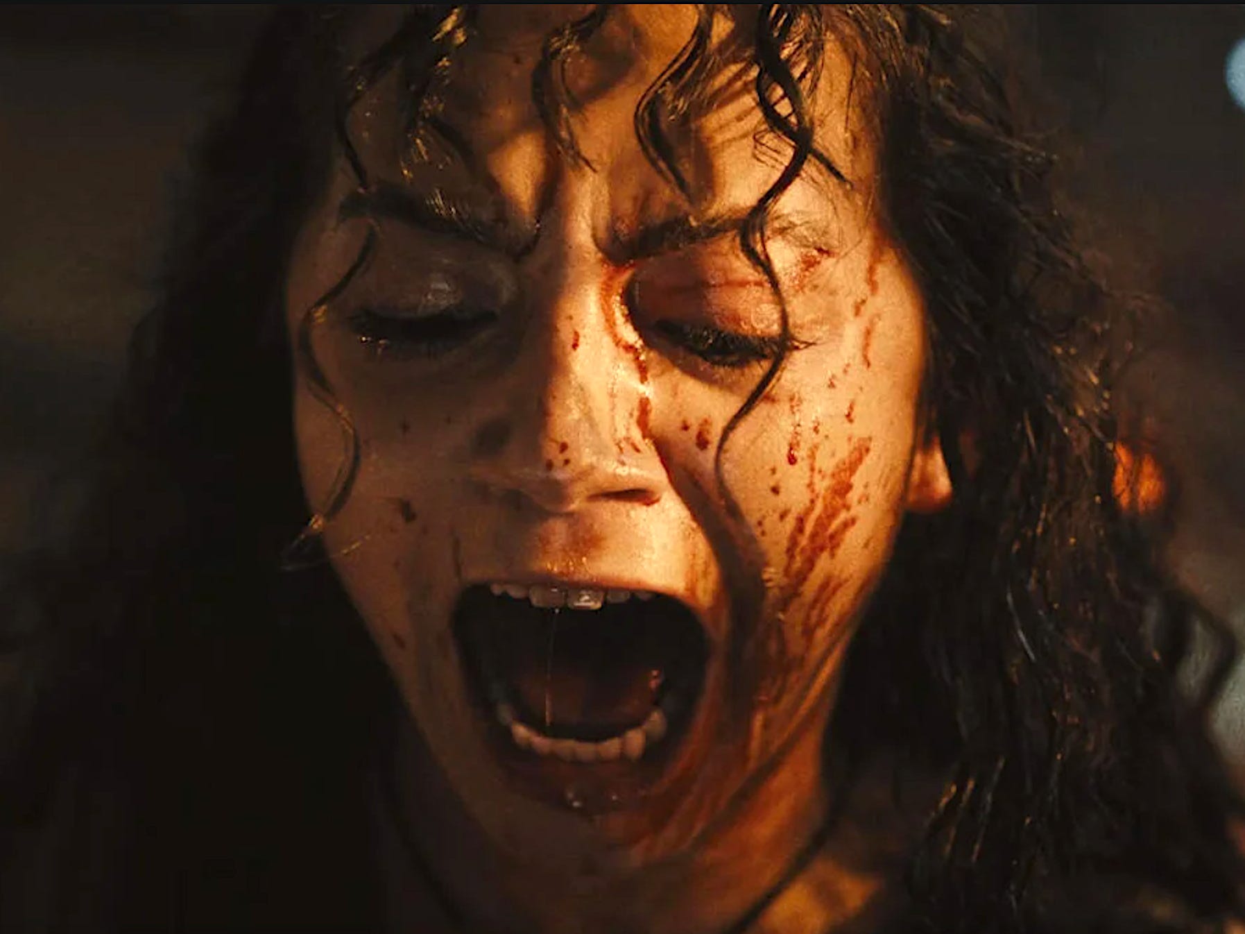 A woman with long black hair looking down while screaming with blood across her face.