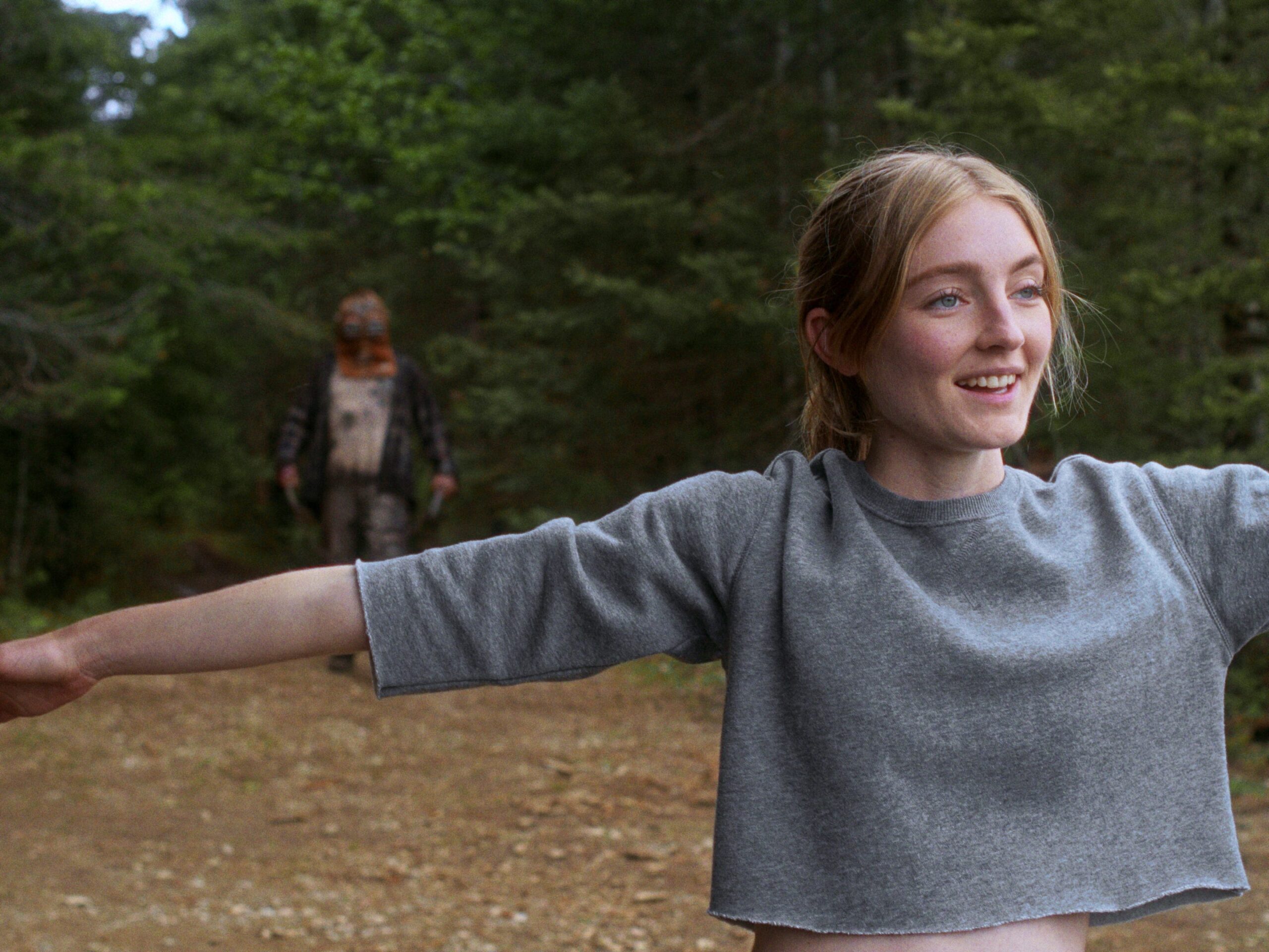 A girl stretching while a monster lurks in the background in a still from "In a Violent Nature"